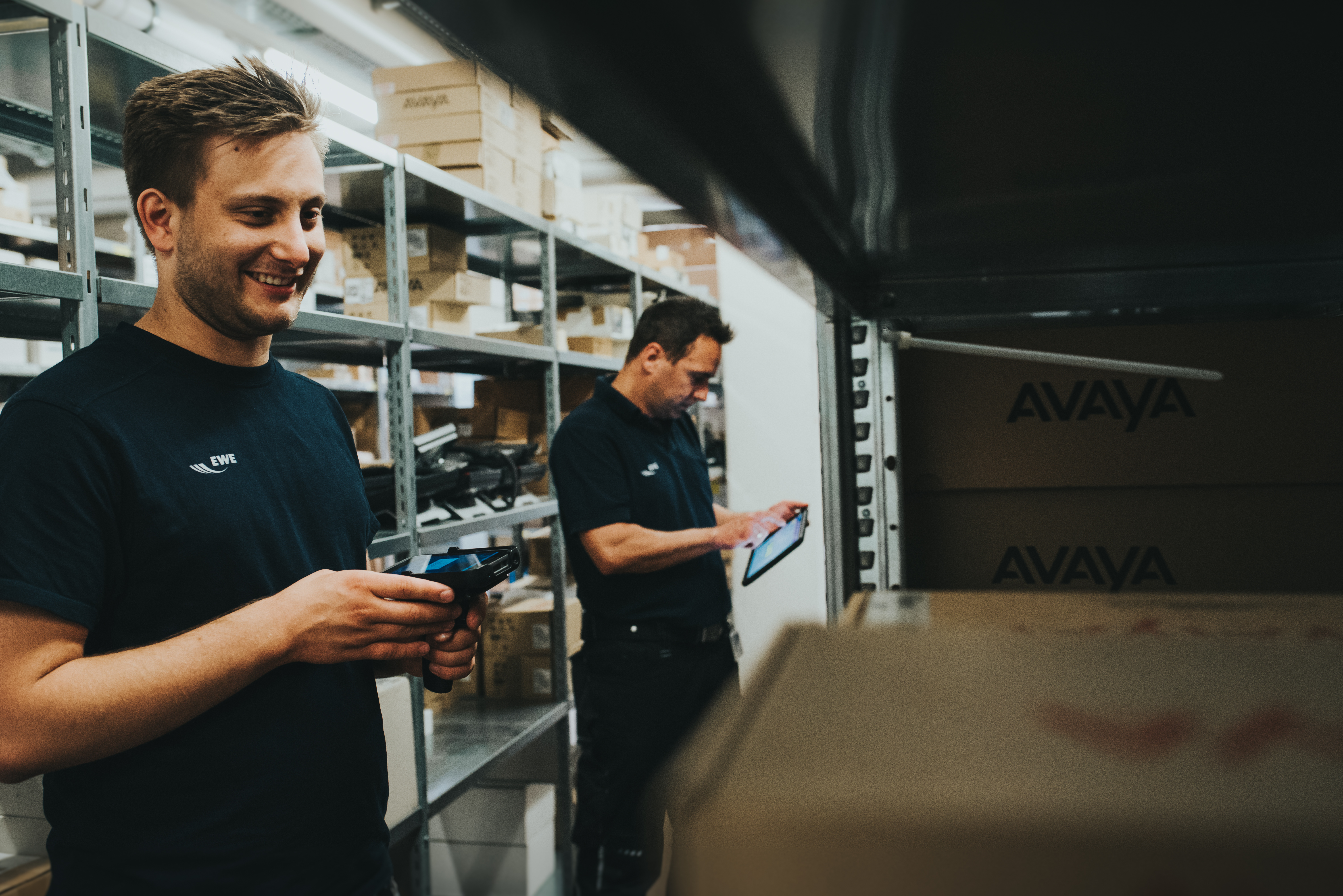 Zwei%20Lagermitarbeiter%20nutzen%20mobile%20Scannerger%E4te%20zwischen%20Regalen%20mit%20Kartons%20und%20zeigen%20digitale%20Bestandsverwaltung%20sowie%20mobile%20Datenerfassung.