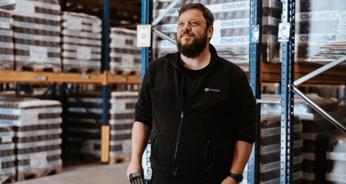 Ein%20Chemex-Lagermitarbeiter%20h%E4lt%20einen%20mobilen%20Barcode-Scanner%20in%20der%20Hand%20und%20steht%20vor%20gestapelten%20Paletten%20mit%20Chemex-Markenprodukten%20in%20einem%20Hochregallager.