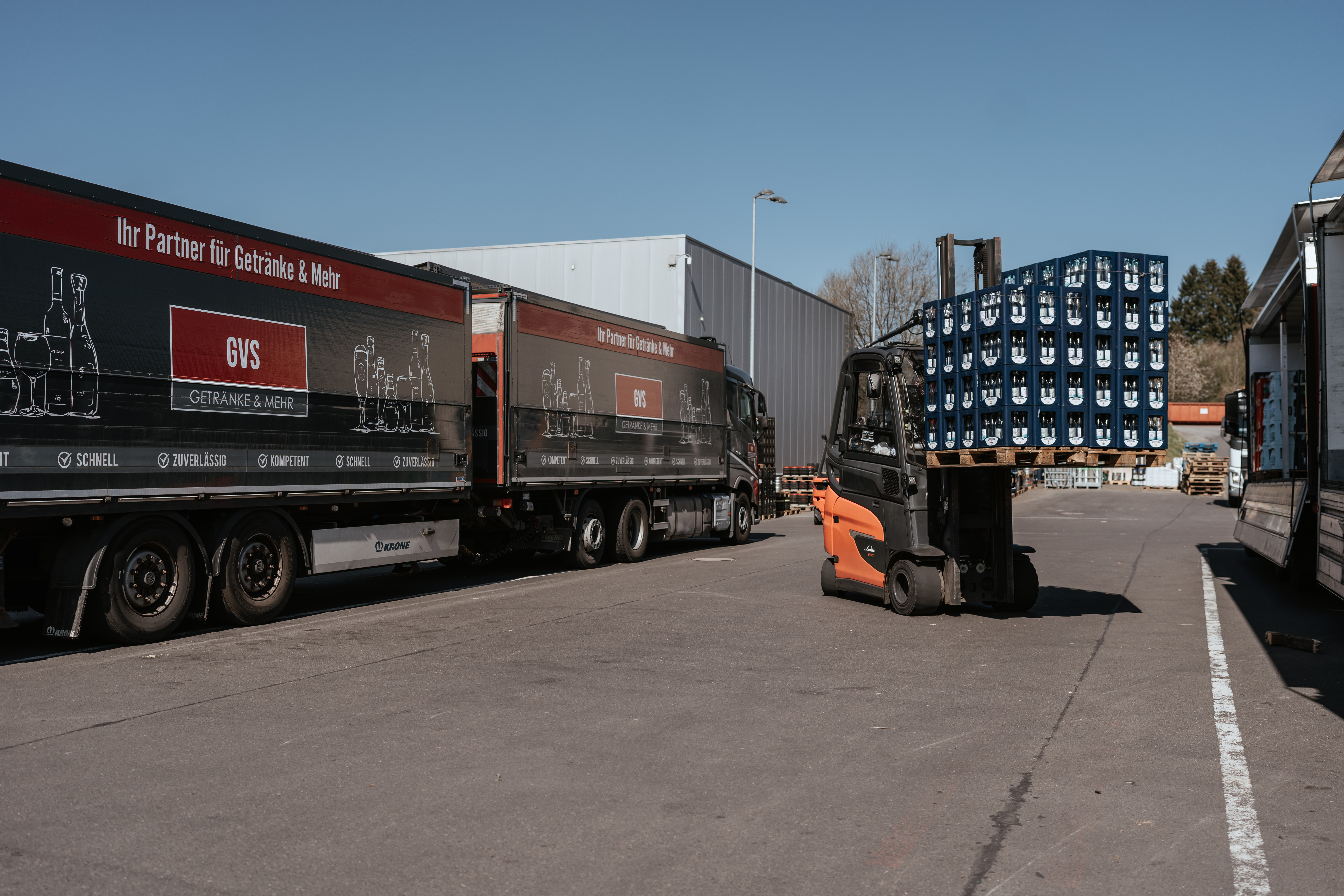 Ein%20Gabelstapler%20l%E4dt%20Getr%E4nkekisten%20auf%20einen%20LKW%20auf%20einem%20Logistikgel%E4nde%2C%20umgeben%20von%20mehreren%20GVS-Getr%E4nketransportern.
